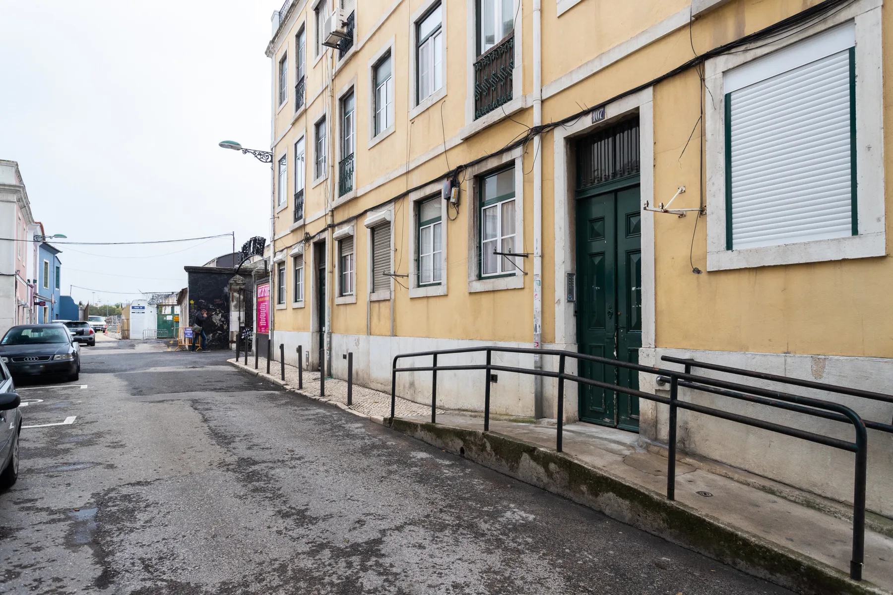 A narrow street runs beside a yellow building with a green entrance.