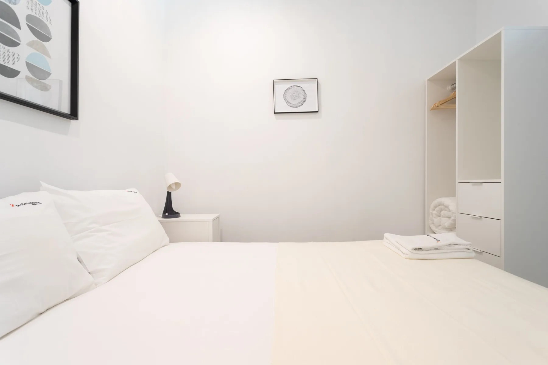 A bright bedroom with white bedding and open shelving.