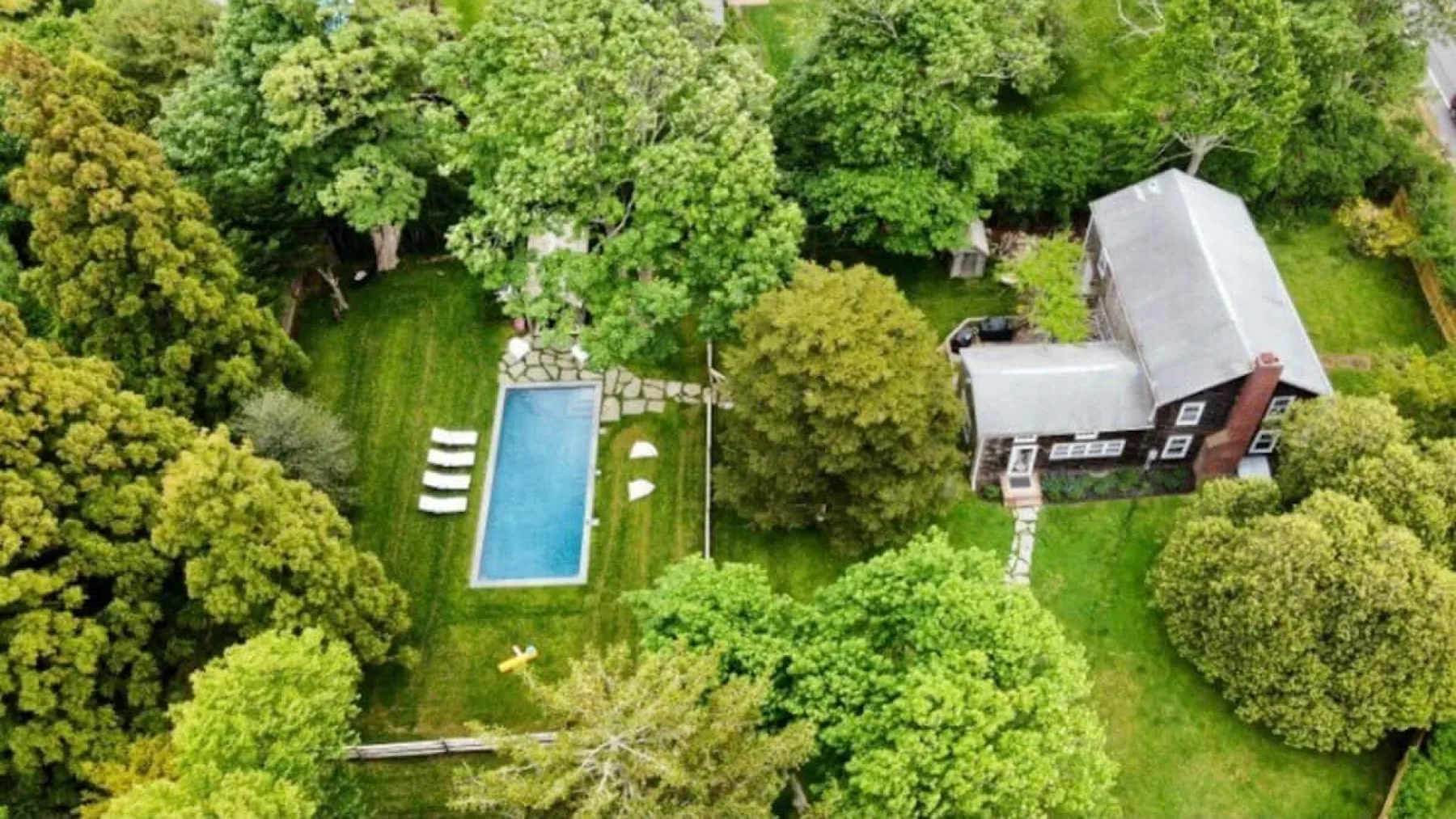 Vista aérea de una casa y una piscina entre árboles verdes.