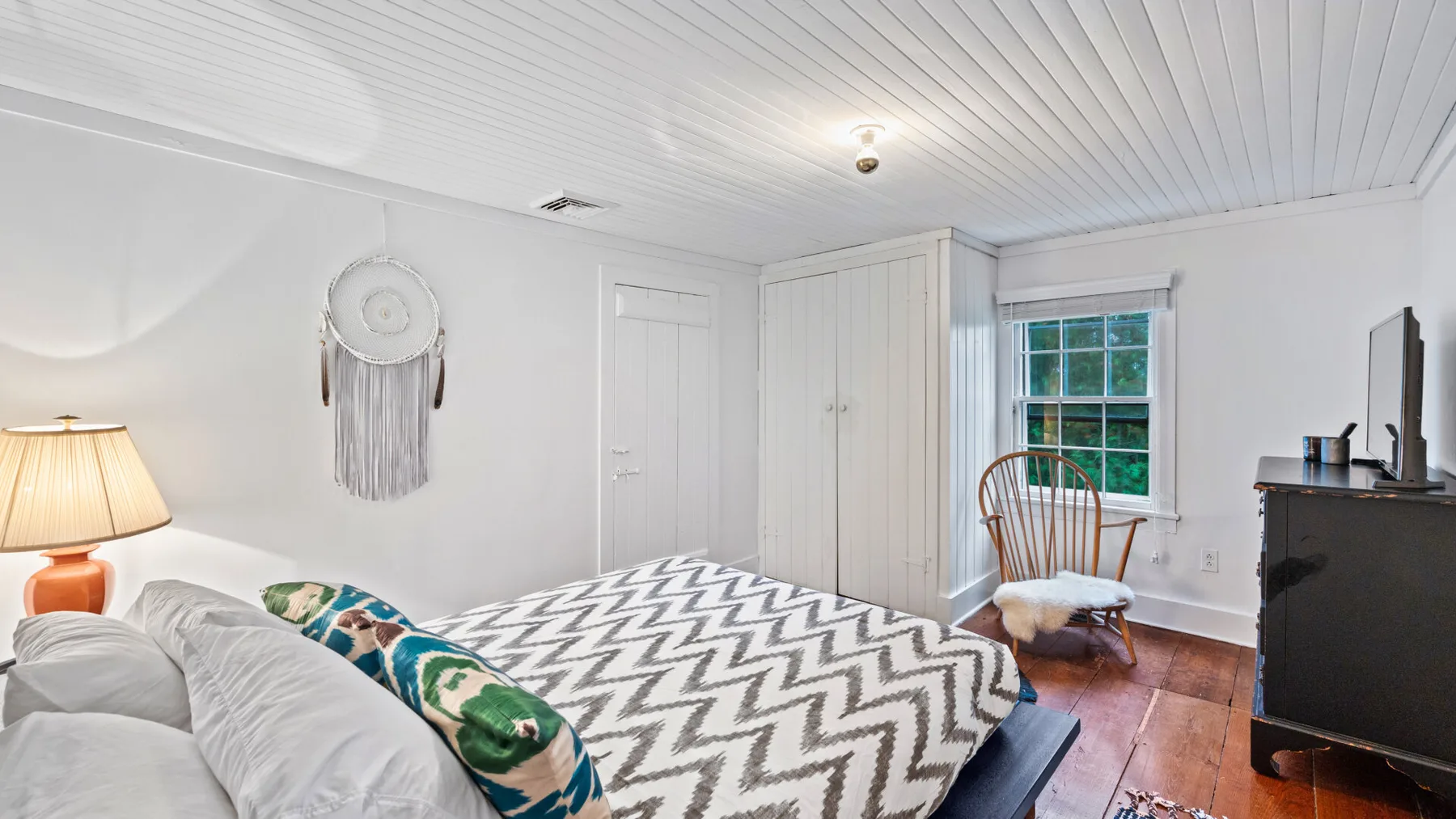 A bedroom with a bed covered by a patterned blanket and a window.