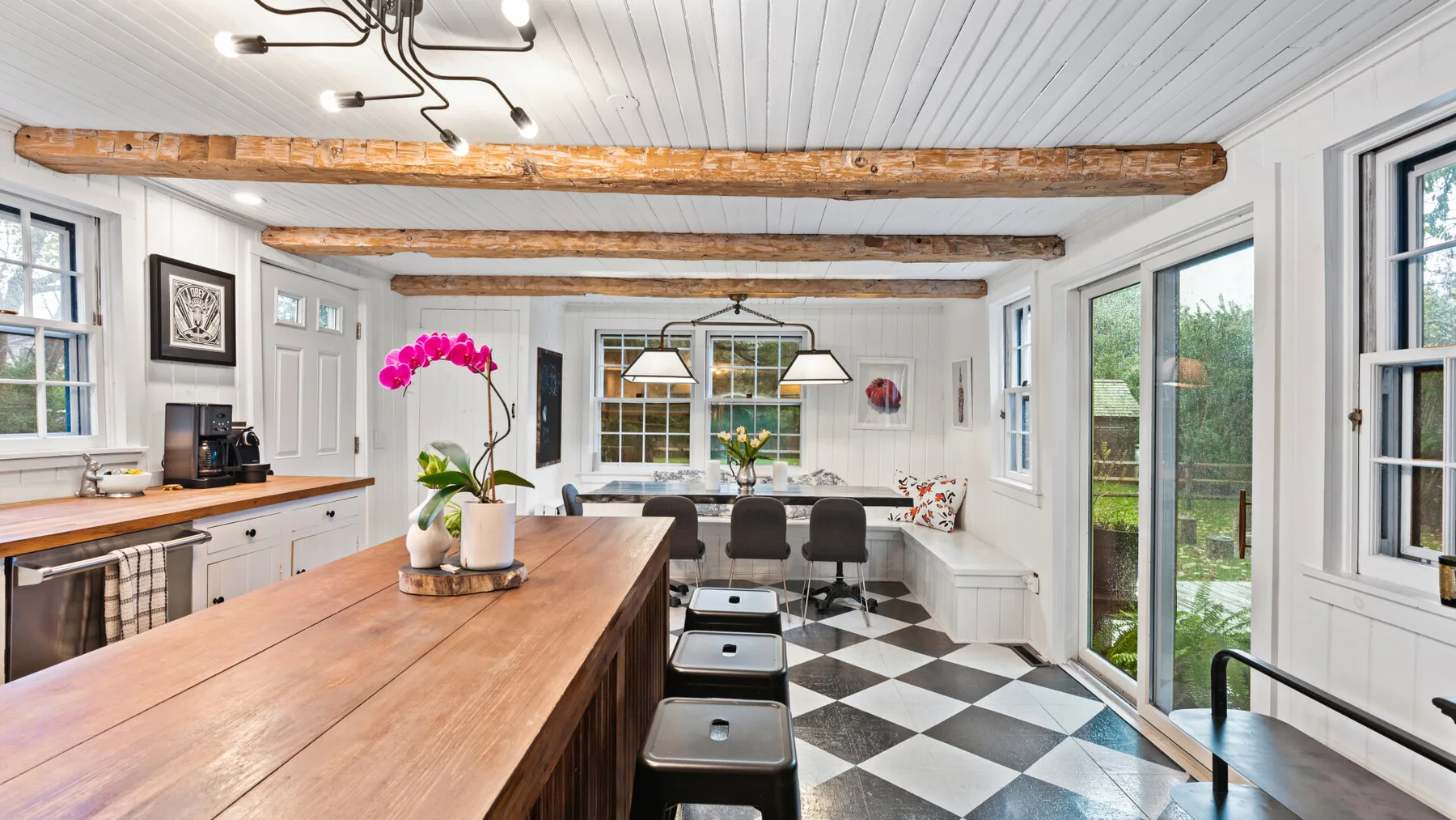 A bright kitchen and dining area with a long wooden island and checkered floor.