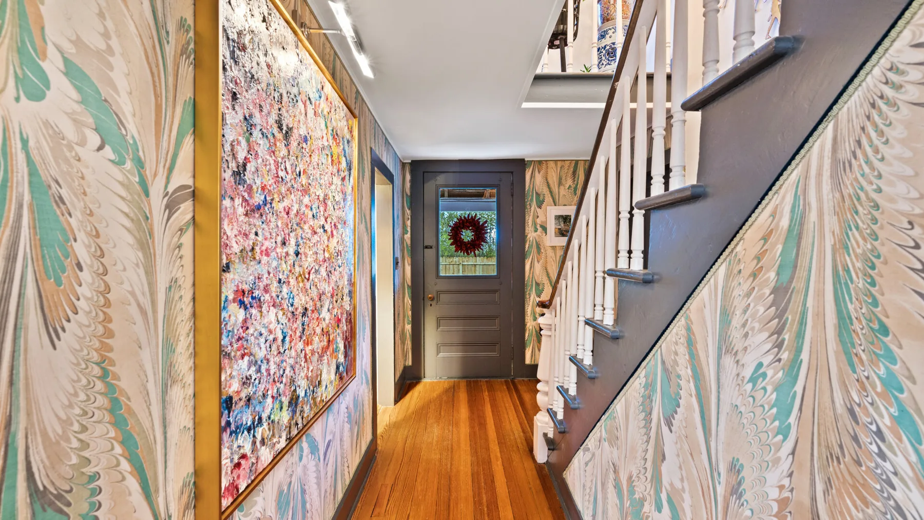A narrow hallway with a wooden staircase and colorful wall art.