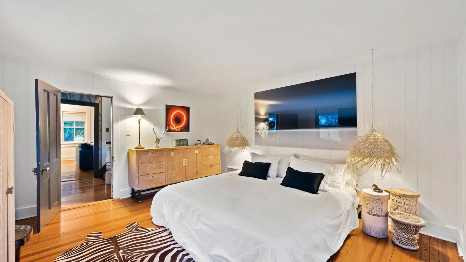 A bedroom with a large bed, wooden dresser, and doorway to an adjoining room.