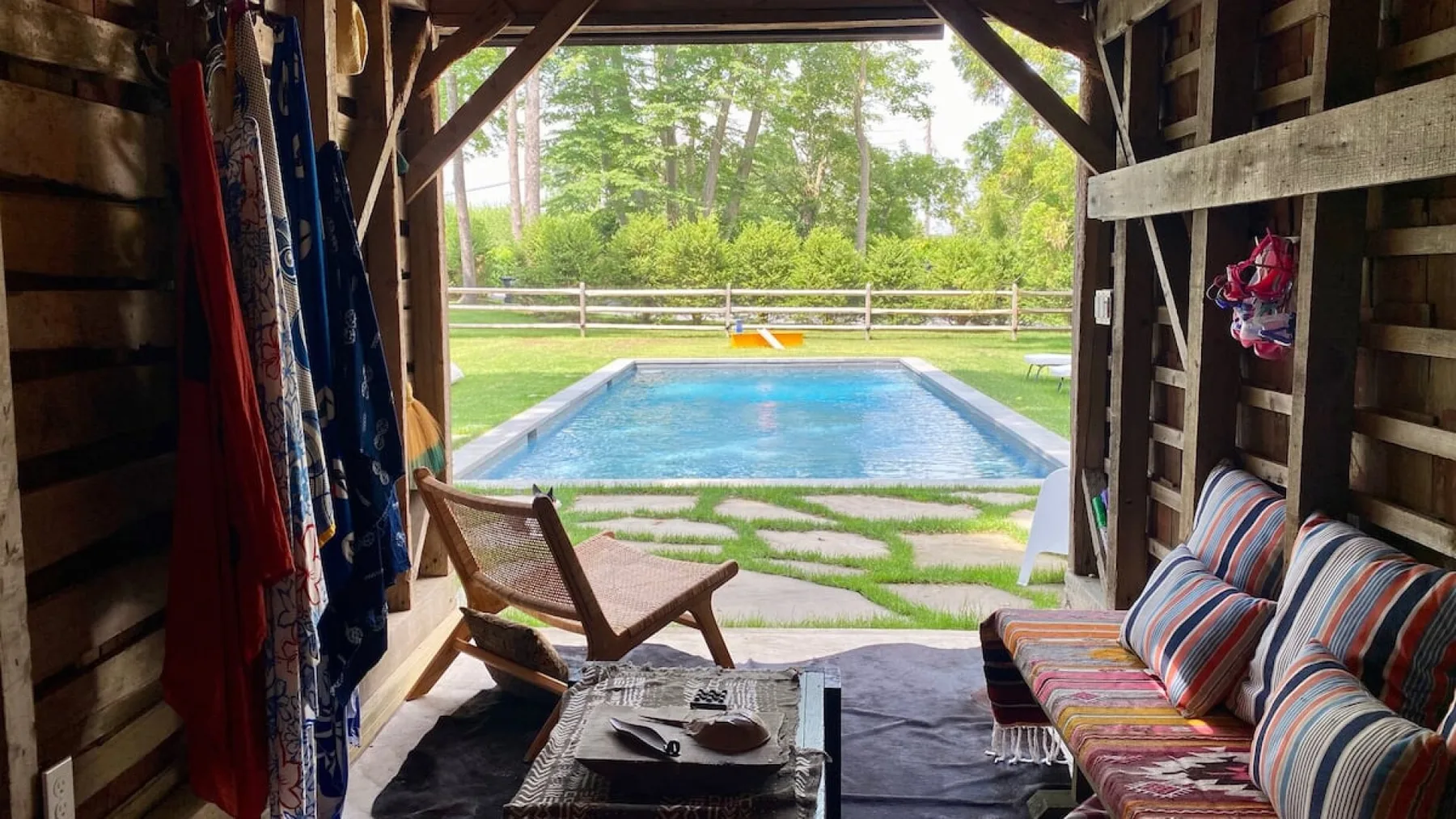A swimming pool is visible beyond a shaded seating area with colorful cushions.