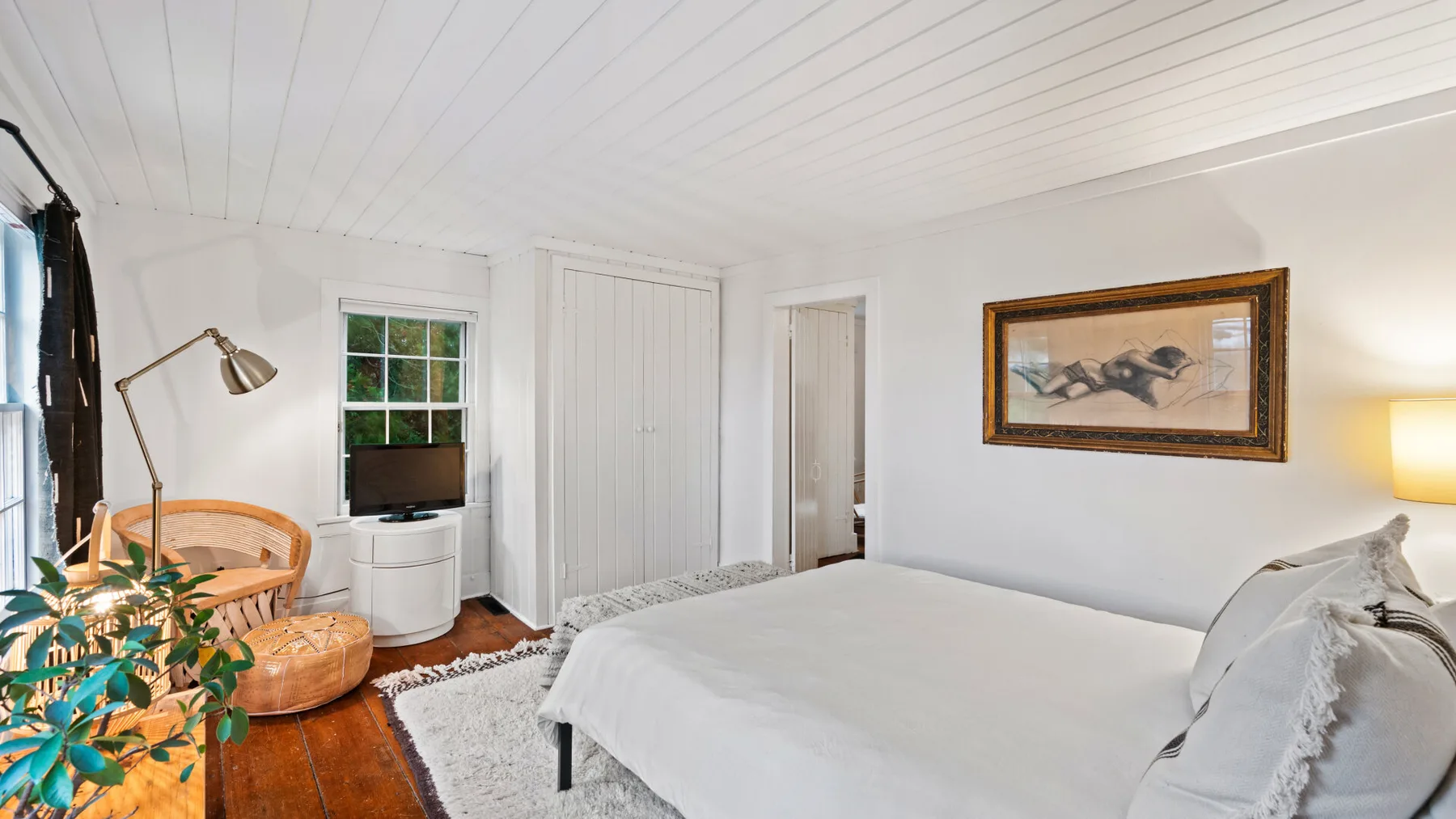 A bright bedroom with a neatly made bed and a television beside the window.