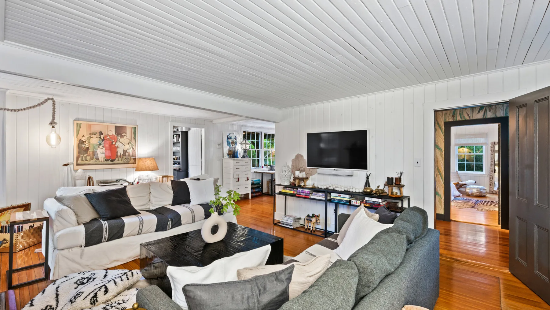 A bright living room with seating, a television, and a doorway opening to another room.