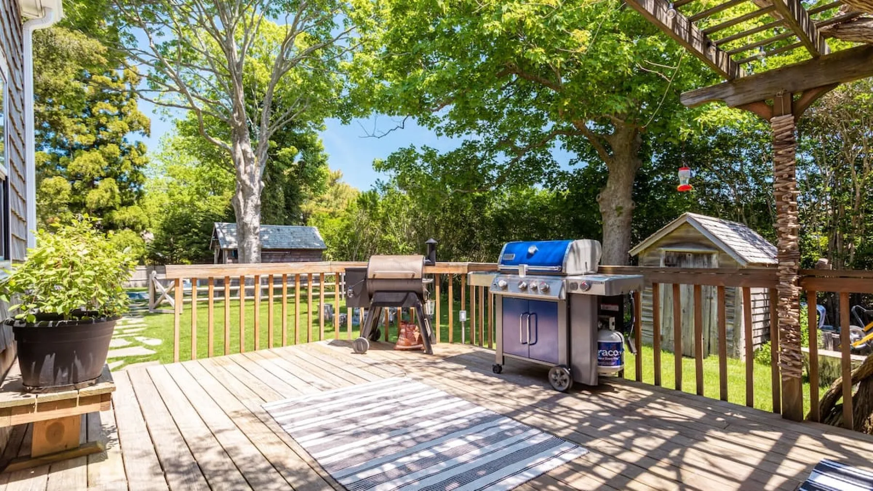 A wooden outdoor deck with a barbecue grill and leafy trees.
