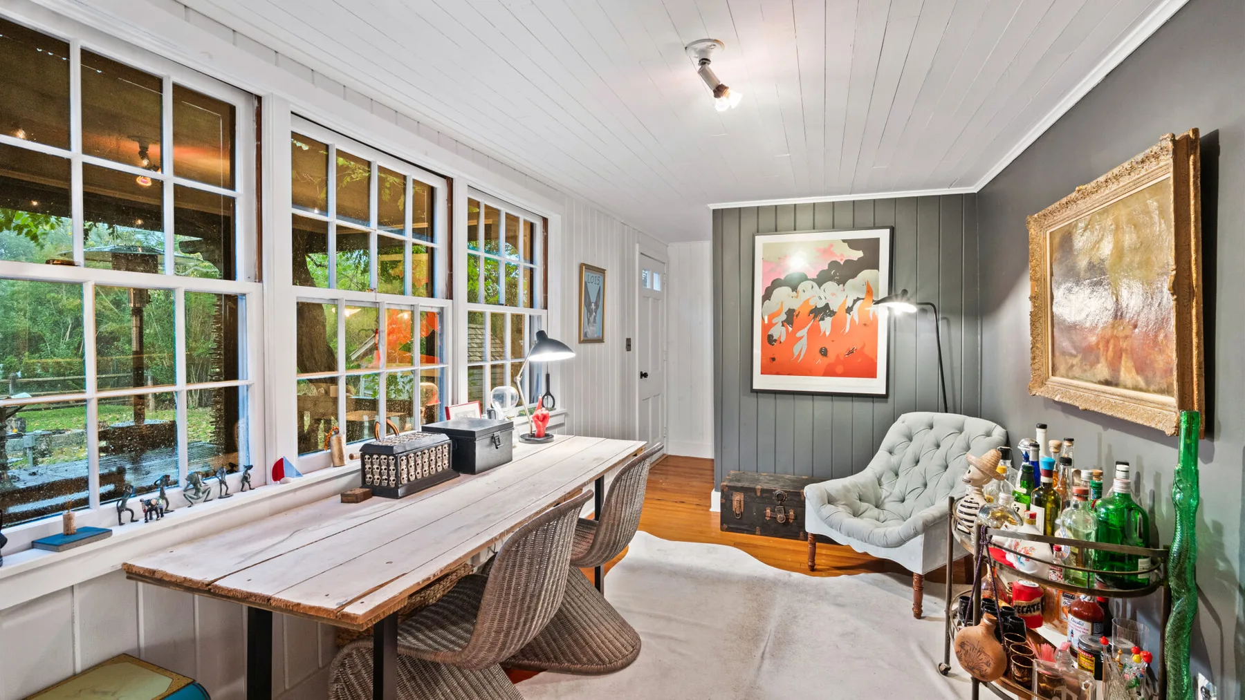 A bright living room with a long table beside large windows and a lounge chair.