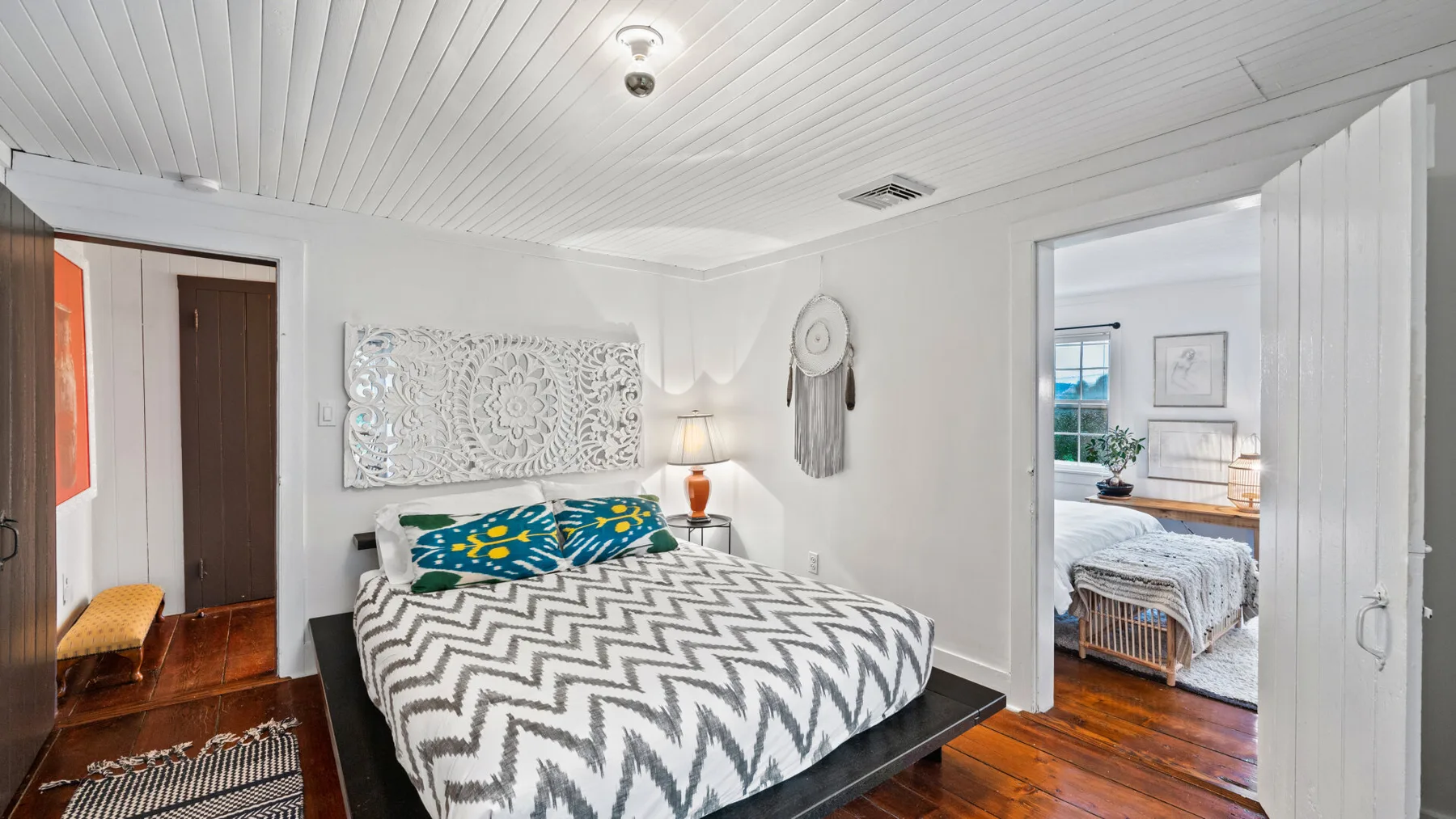 A bedroom with a bed beneath decorative wall art and an open doorway to another room.