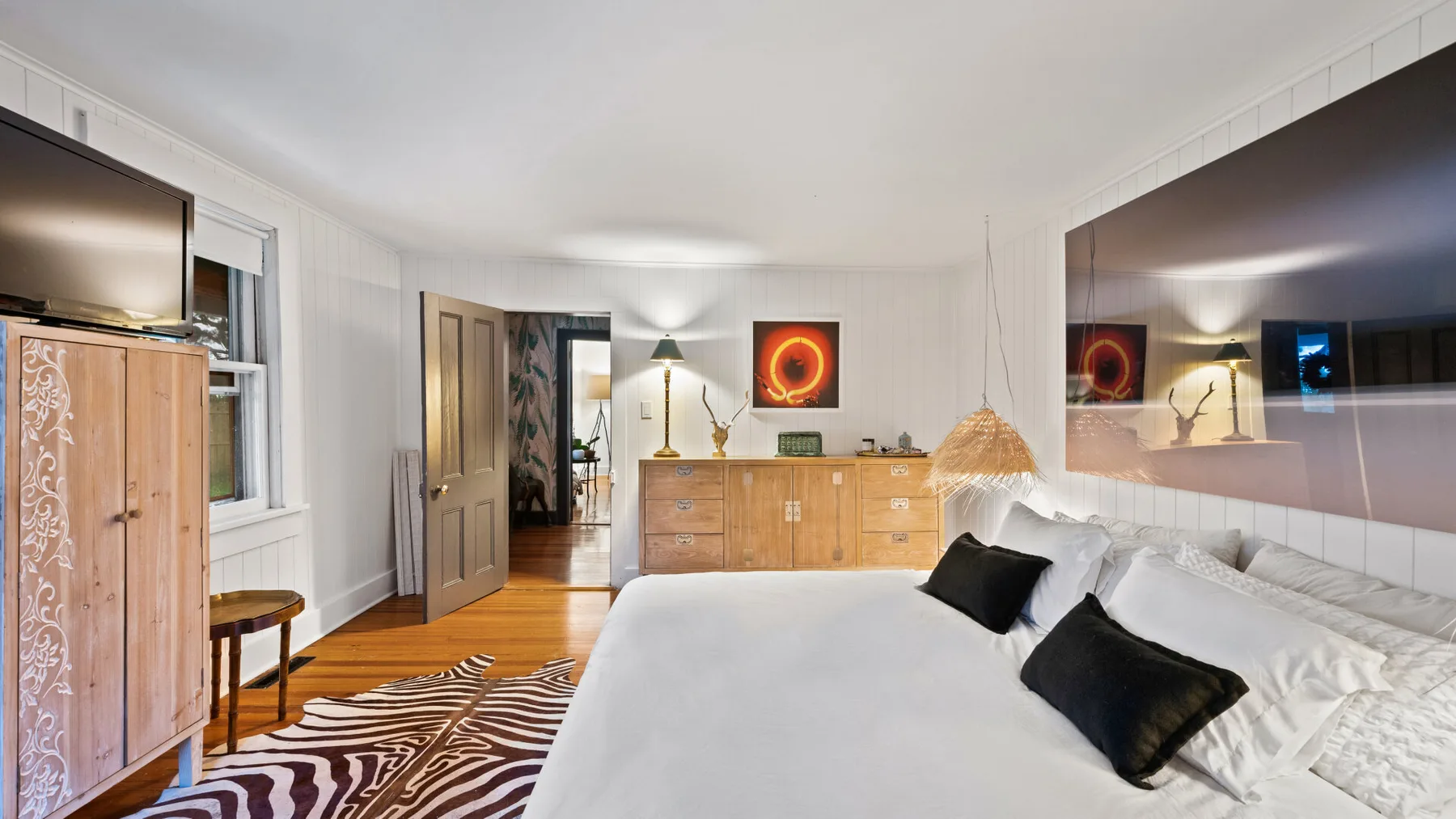 A bedroom with a large bed, wooden dresser, and wall-mounted television.