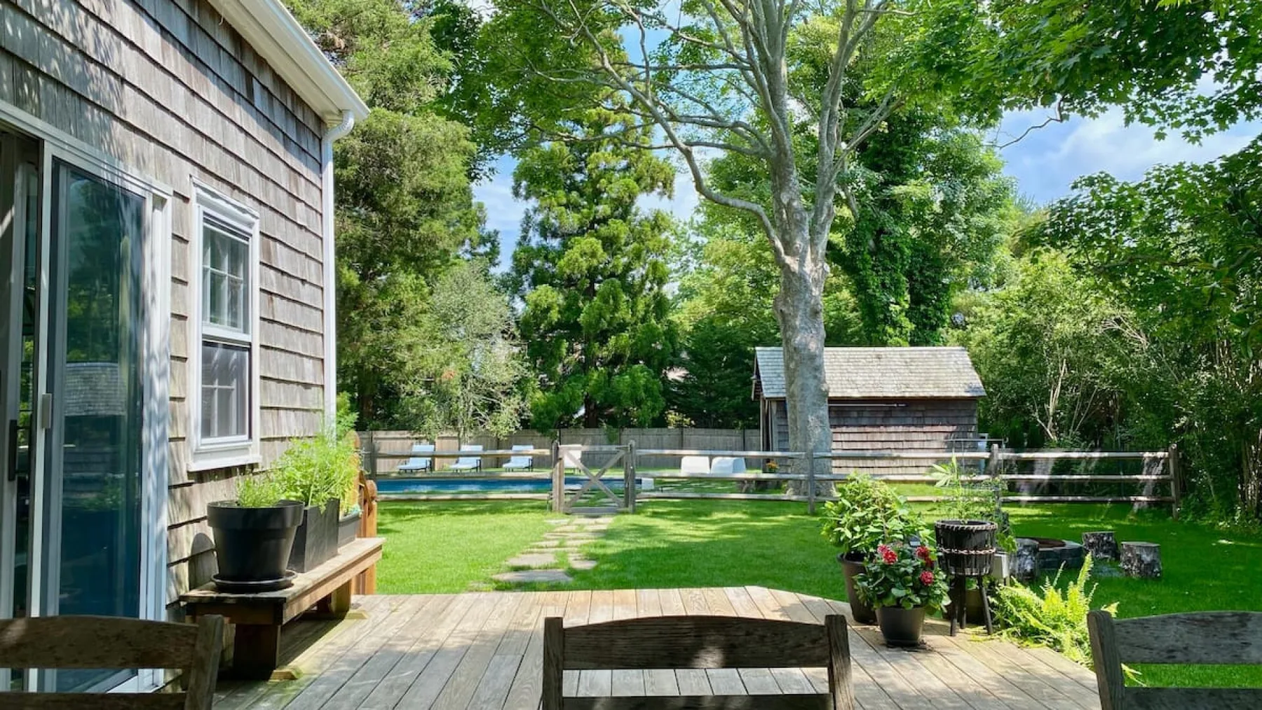 A backyard garden with a wooden deck, green lawn, and mature trees.