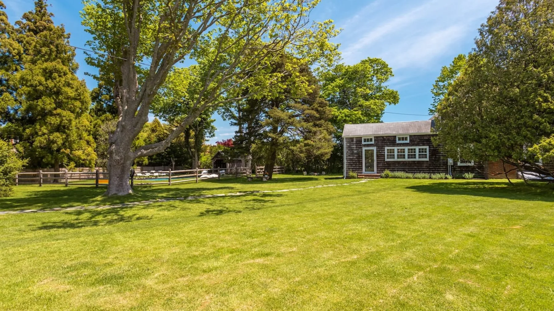 A grassy lawn extends toward a small building beneath leafy trees.