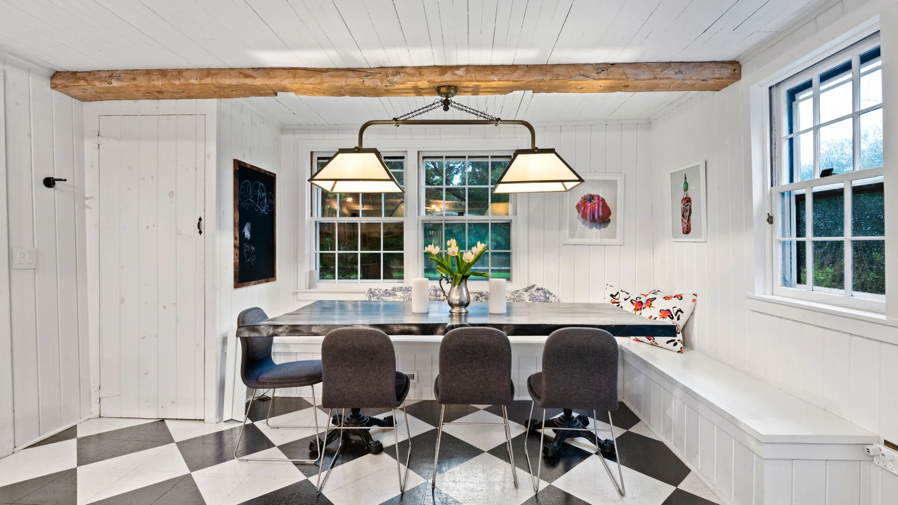 A bright dining area with a long table, dark seating, and large windows.