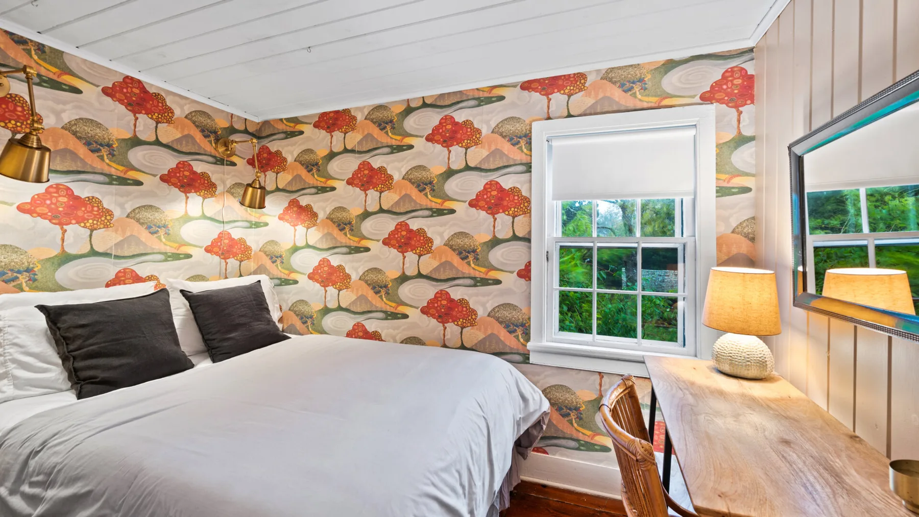 A bedroom with a bed, patterned walls, and a desk beside the window.
