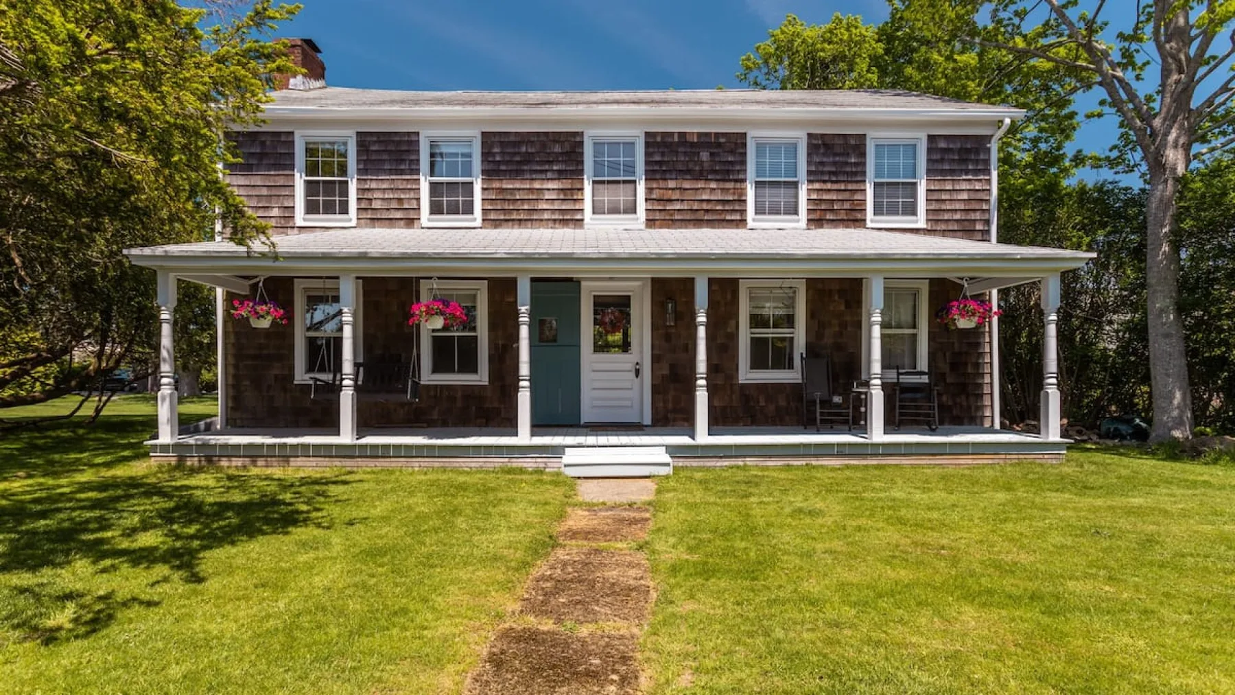 A two-story house with a covered porch stands behind a grassy lawn.