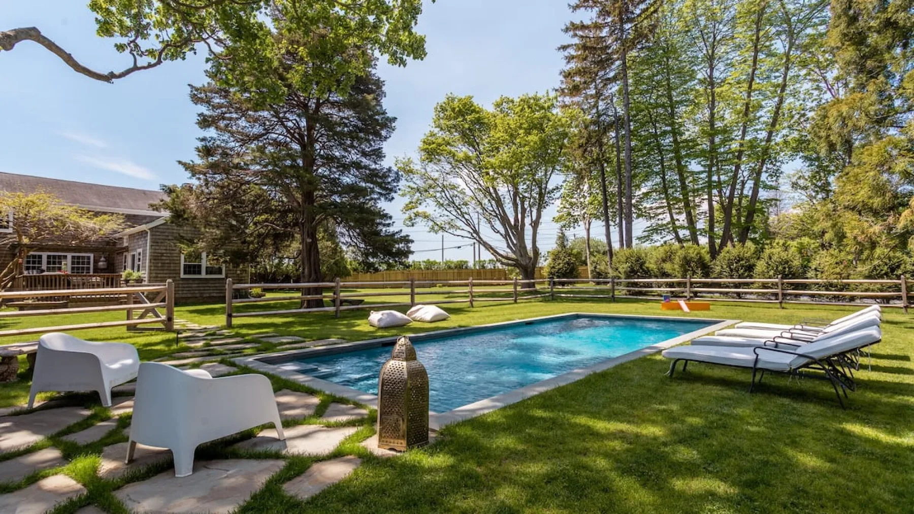 An outdoor swimming pool is surrounded by lawn, lounge seating, and trees.