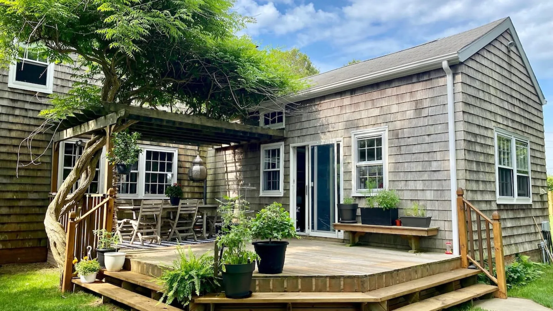 A house with a wooden deck, outdoor seating, and leafy trees.