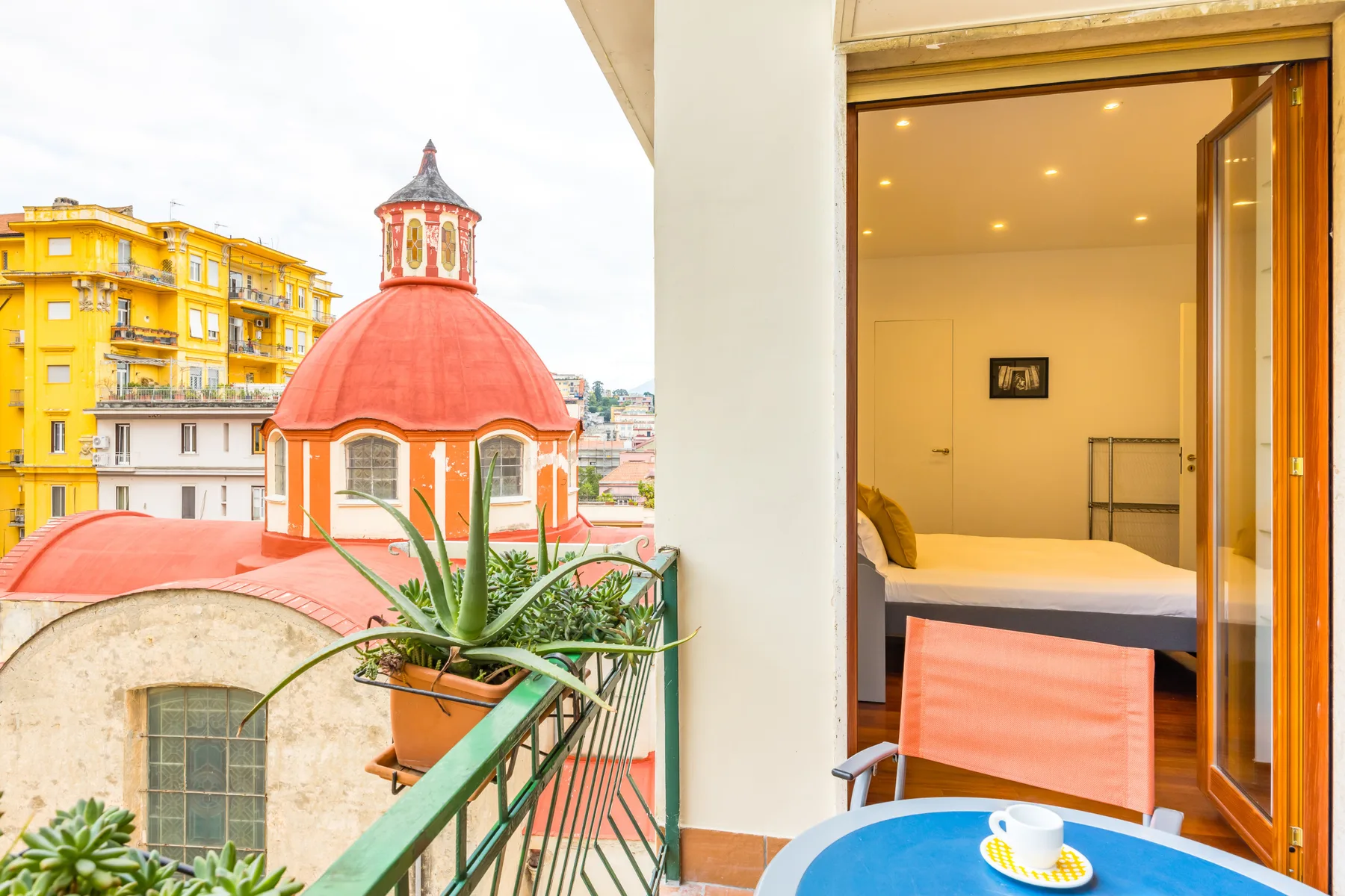 A balcony with seating overlooks a distinctive red-domed building and surrounding city rooftops.