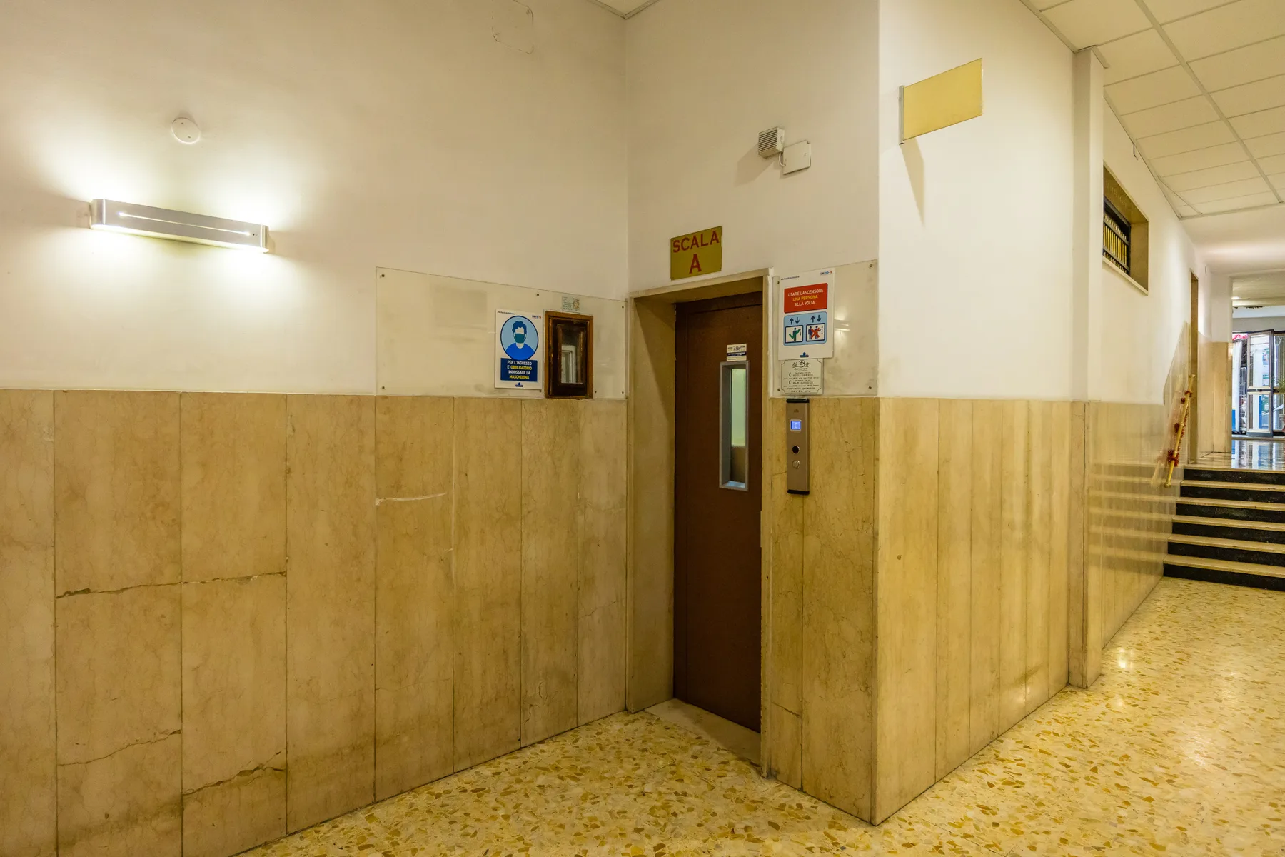 A tiled hallway with a brown elevator door and wall-mounted signs.