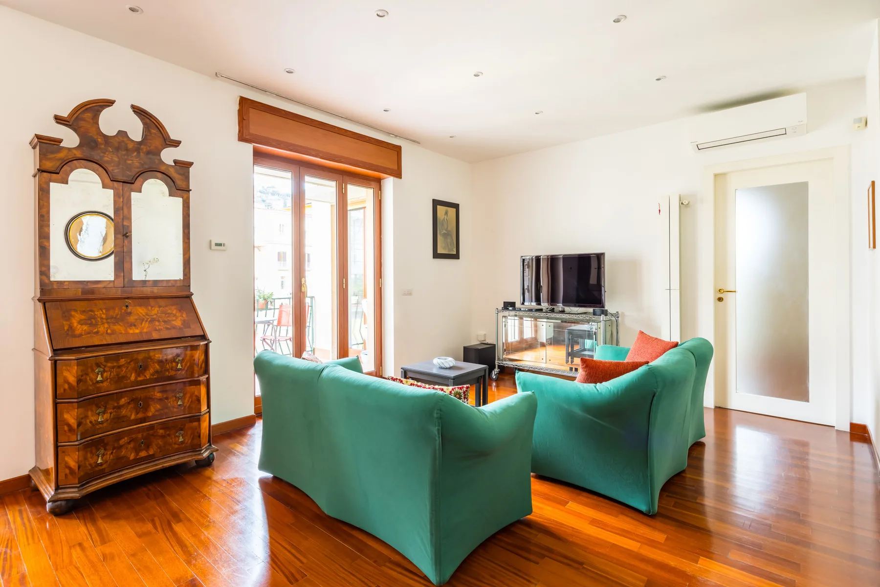 A living room with green seating, a television, and a wooden cabinet.