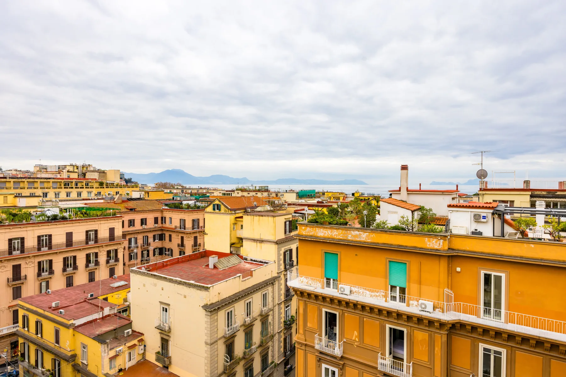 Rooftops and apartment buildings fill an urban cityscape beneath a cloudy sky.