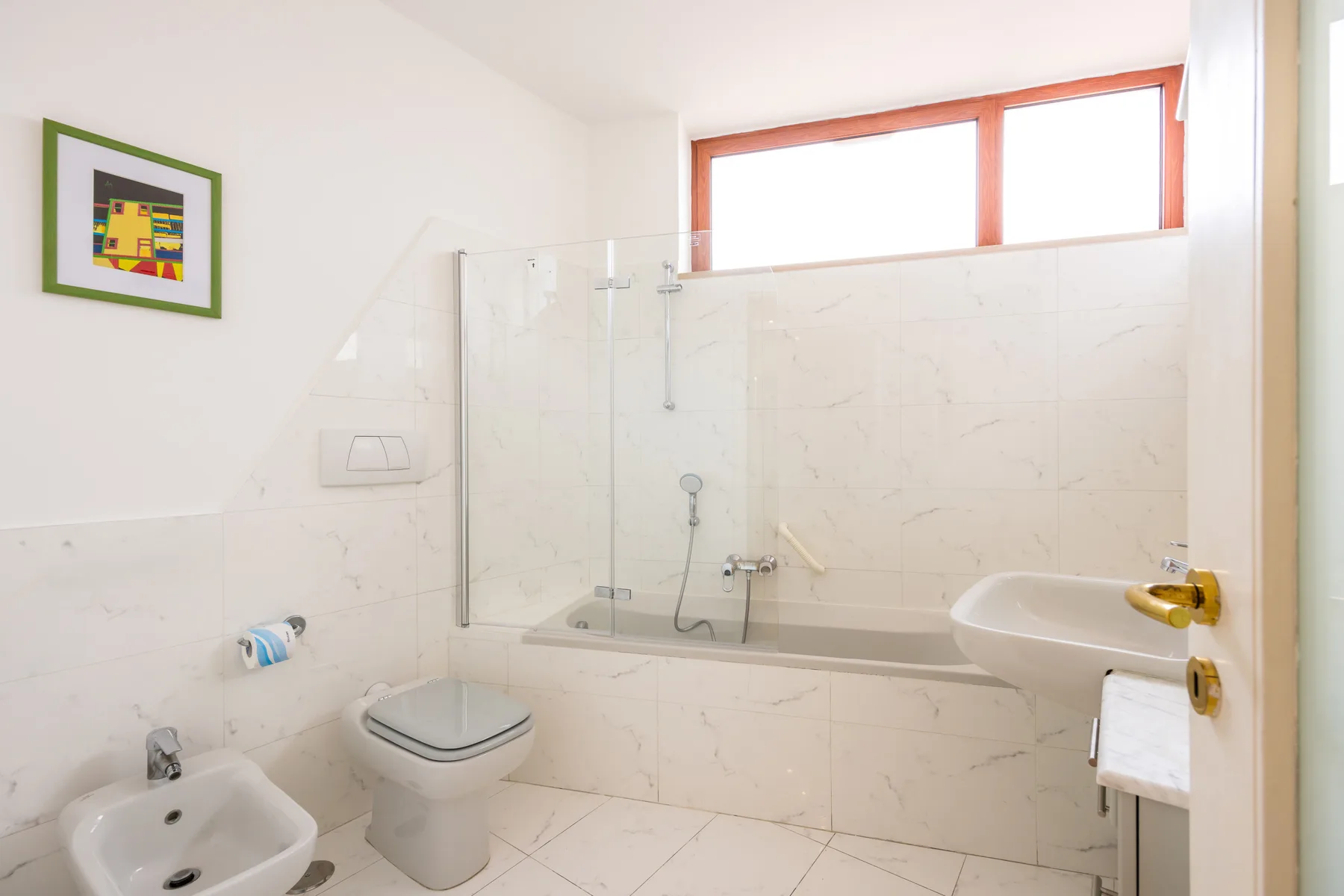 A bright bathroom with a bathtub, glass shower screen, and white fixtures.