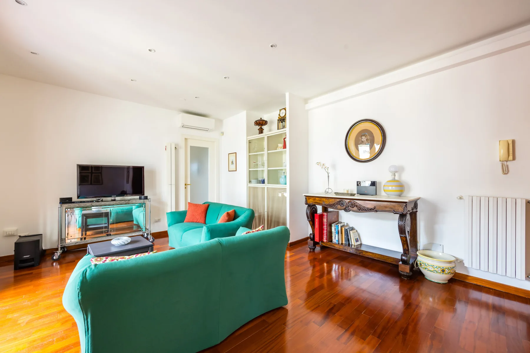 A bright living room with green seating, a television, and polished wood flooring.