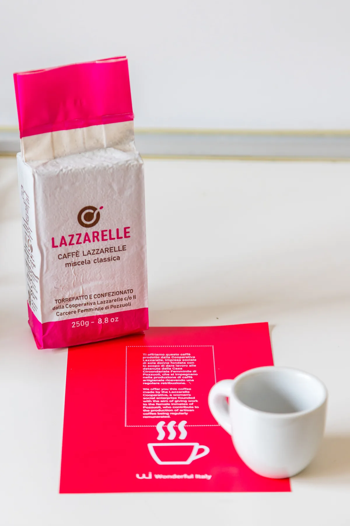 A coffee packet and white cup sit on a bright pink mat.