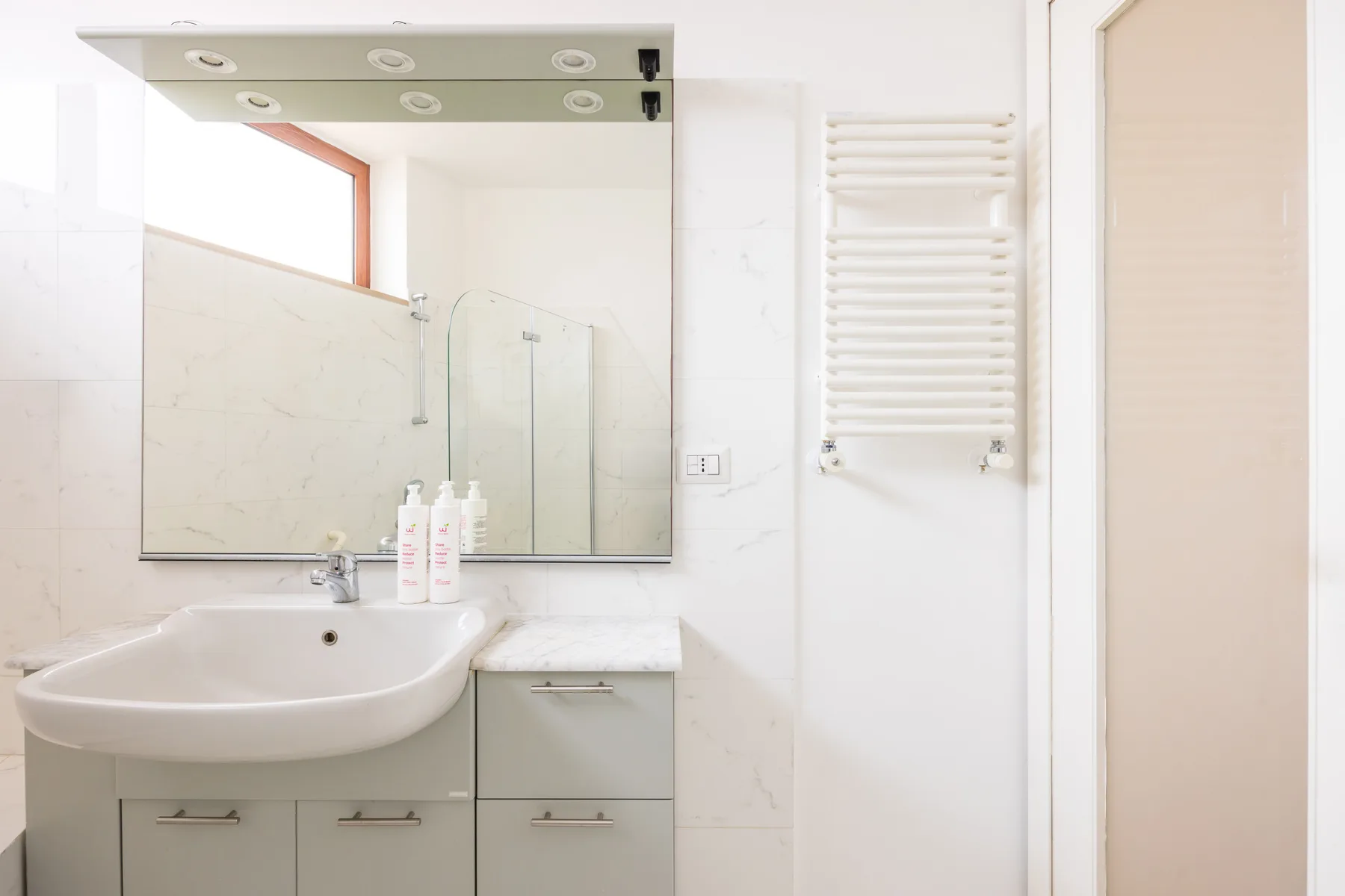A bright bathroom with a sink, mirror, and wall-mounted towel radiator.