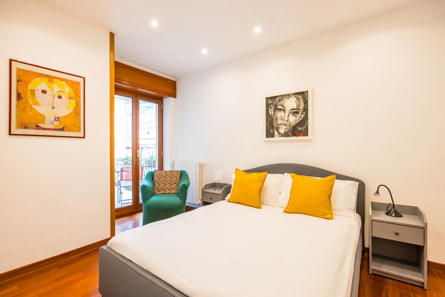 A bright bedroom with a large bed, colorful pillows, and framed artwork.