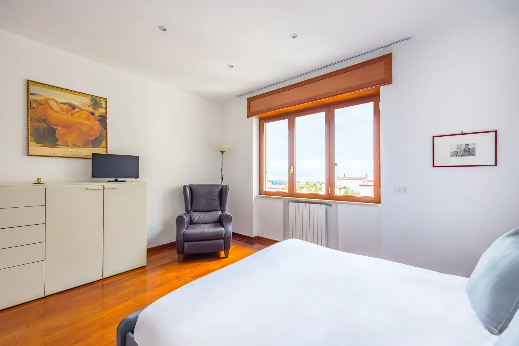 A bright bedroom with a bed, window, and seating.