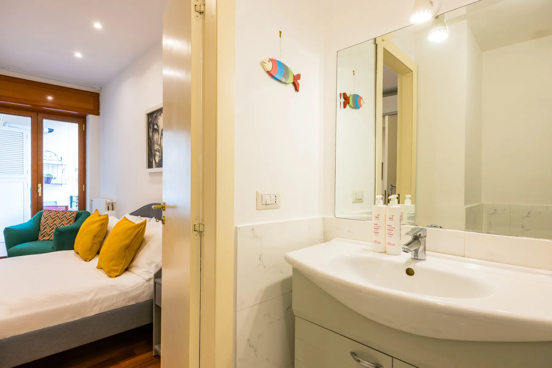 A bedroom beside a bathroom vanity, with a bed and wall mirror visible.