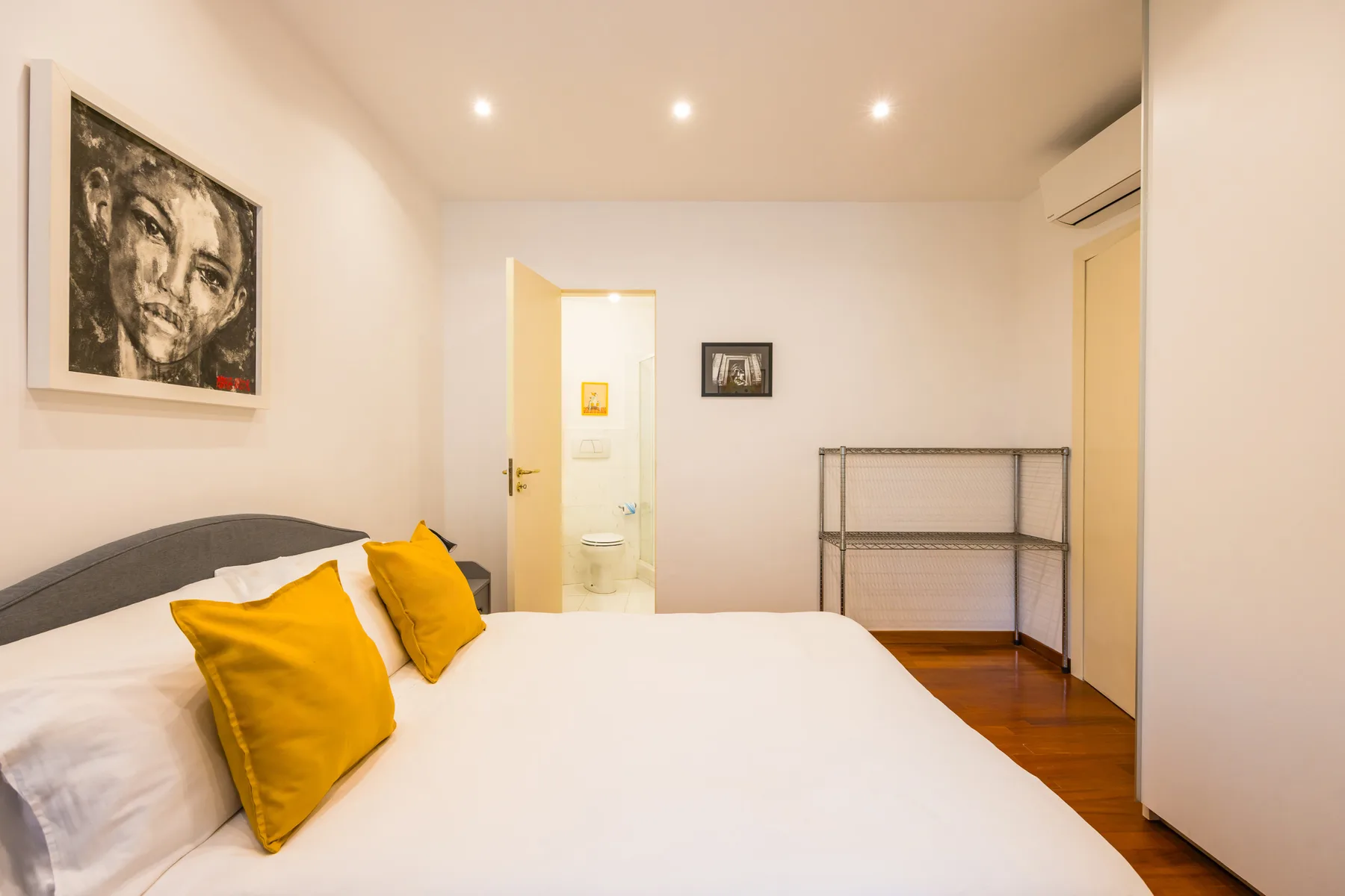 A bedroom with a bed, yellow pillows, and framed artwork on the wall.