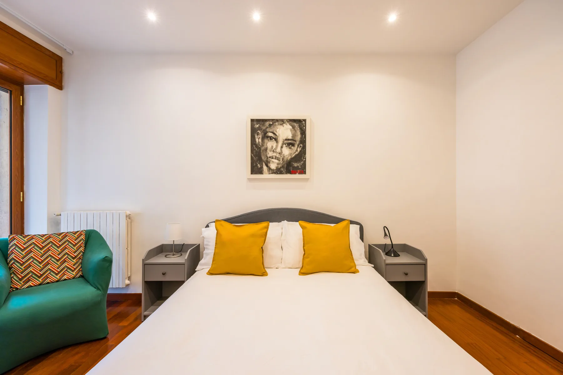 A bedroom with a bed, yellow pillows, and a framed picture on the wall.