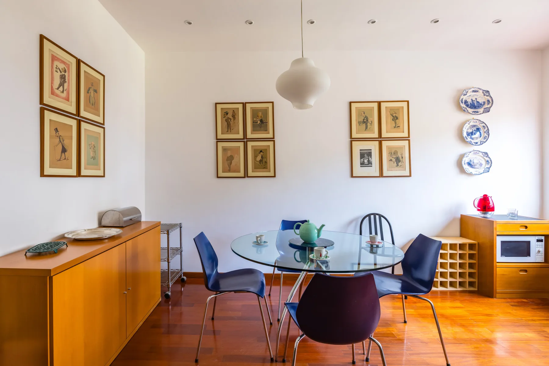 A dining area with a round glass table, chairs, and framed artwork on the walls.