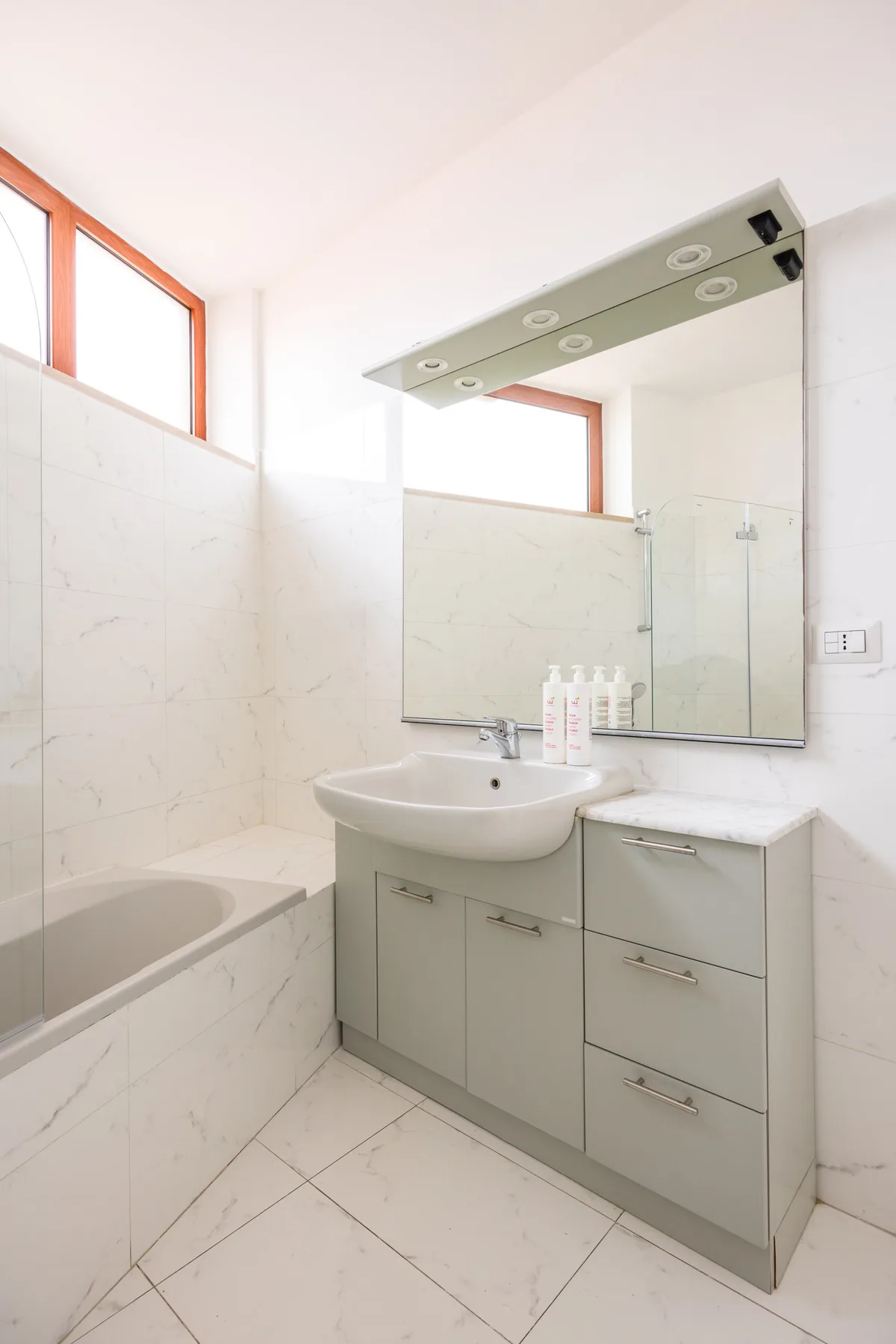 A bright bathroom with a bathtub, sink, and mirrored vanity.