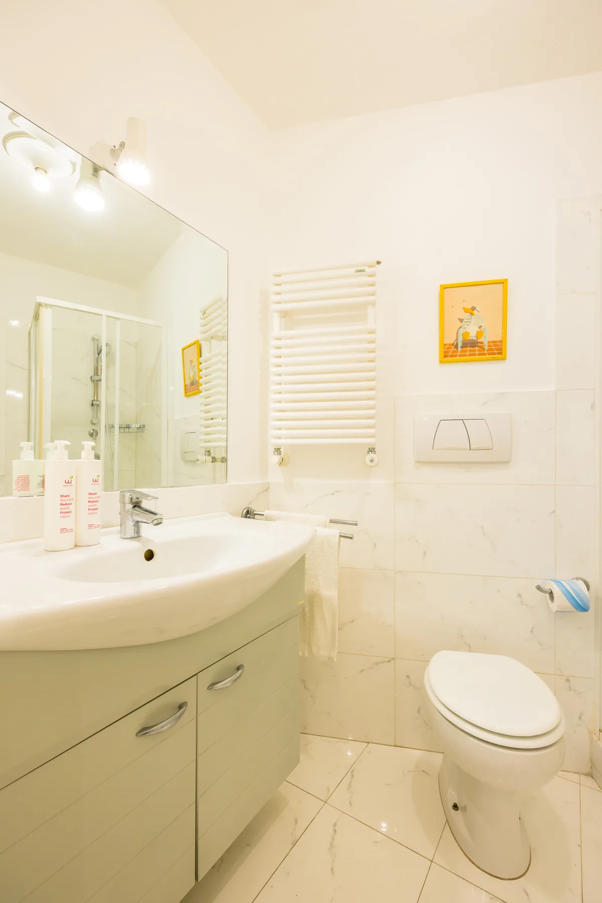 A bright bathroom with a sink, toilet, and wall-mounted towel warmer.