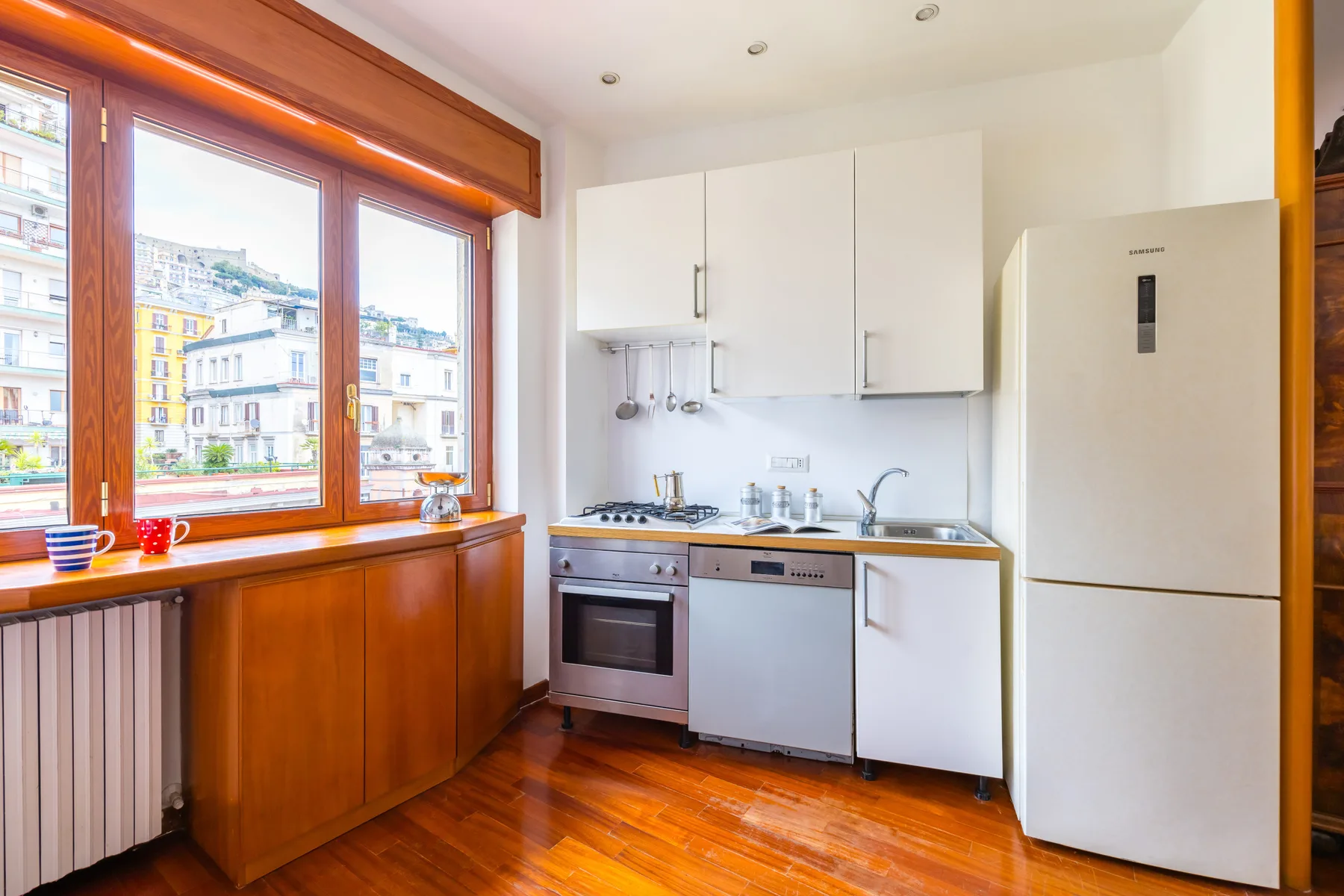 A bright kitchen with white cabinets, a refrigerator, and wooden flooring.