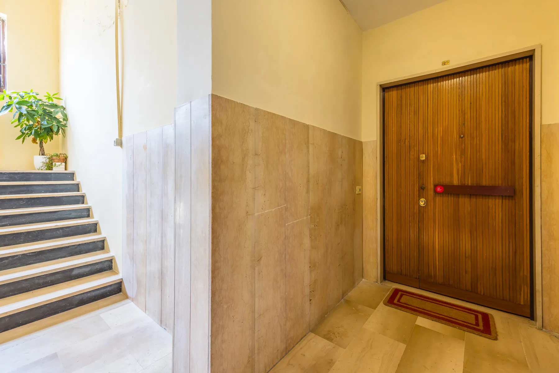 An indoor stairwell with tiled steps beside a wooden entrance door.