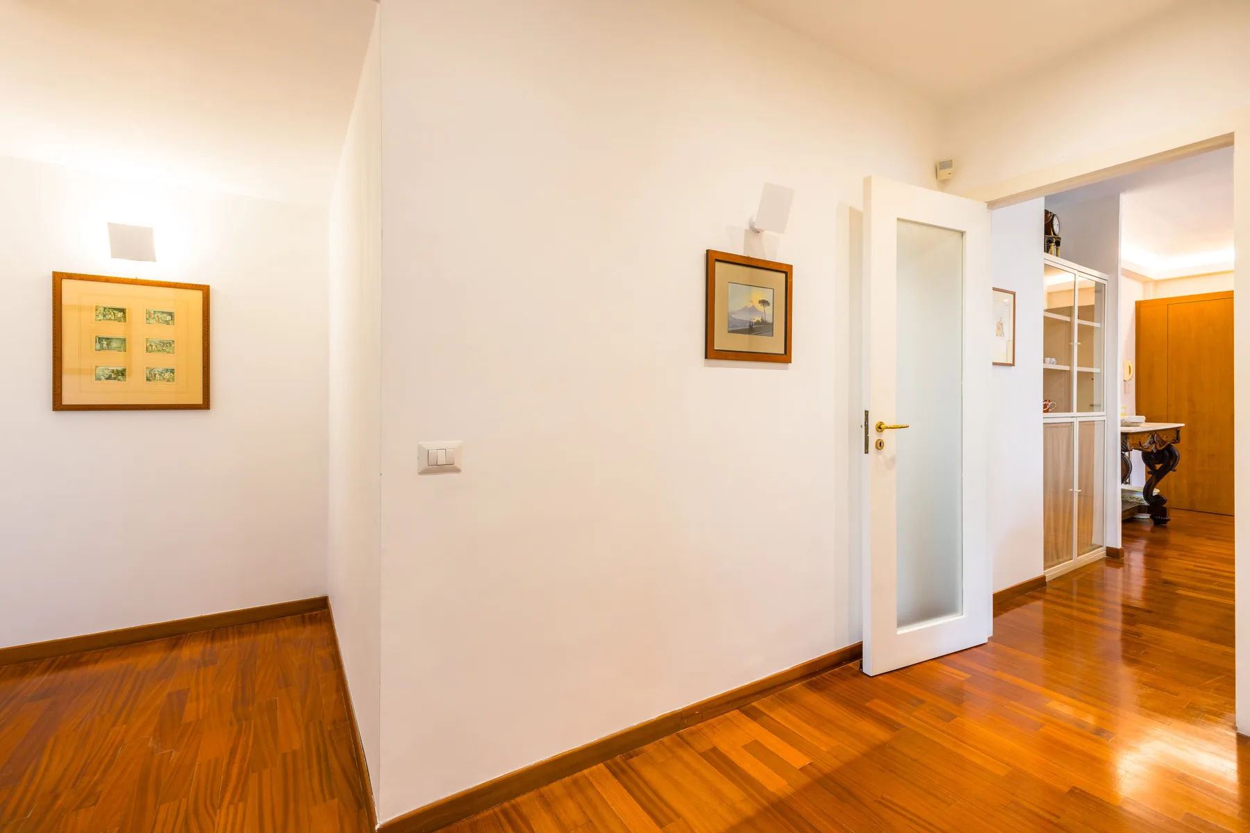 A bright hallway with an open door leading to a room with wooden flooring.