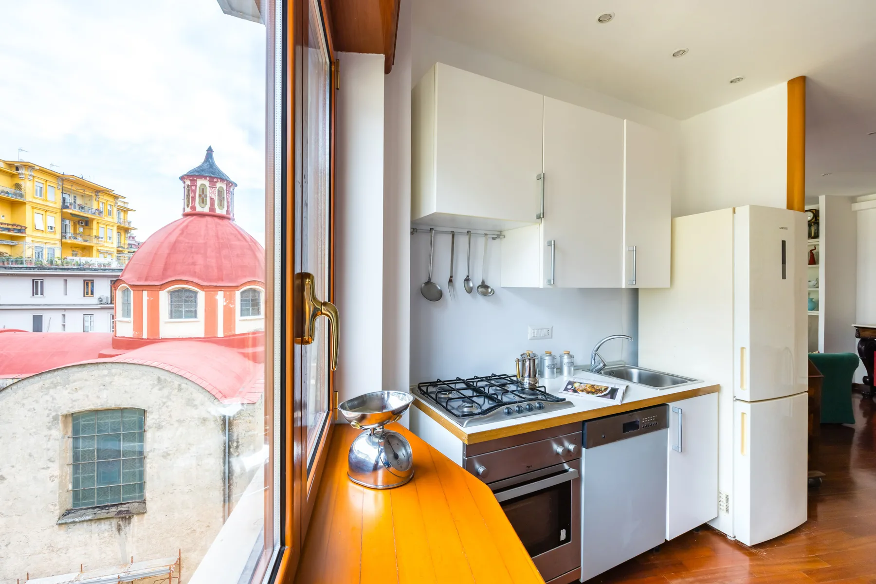 A bright kitchen with a gas cooktop and large windows overlooking nearby buildings.