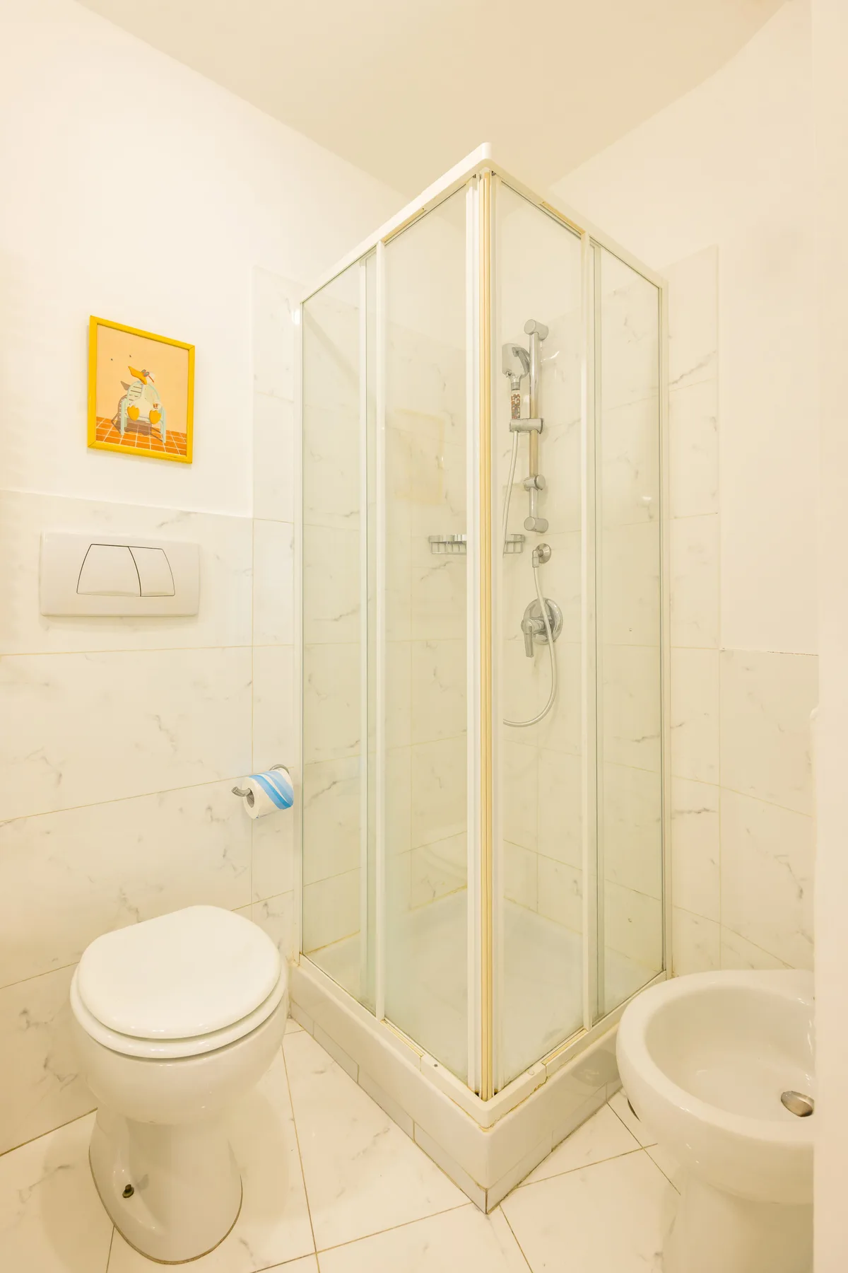 A tiled bathroom with a glass shower, toilet, and washbasin.