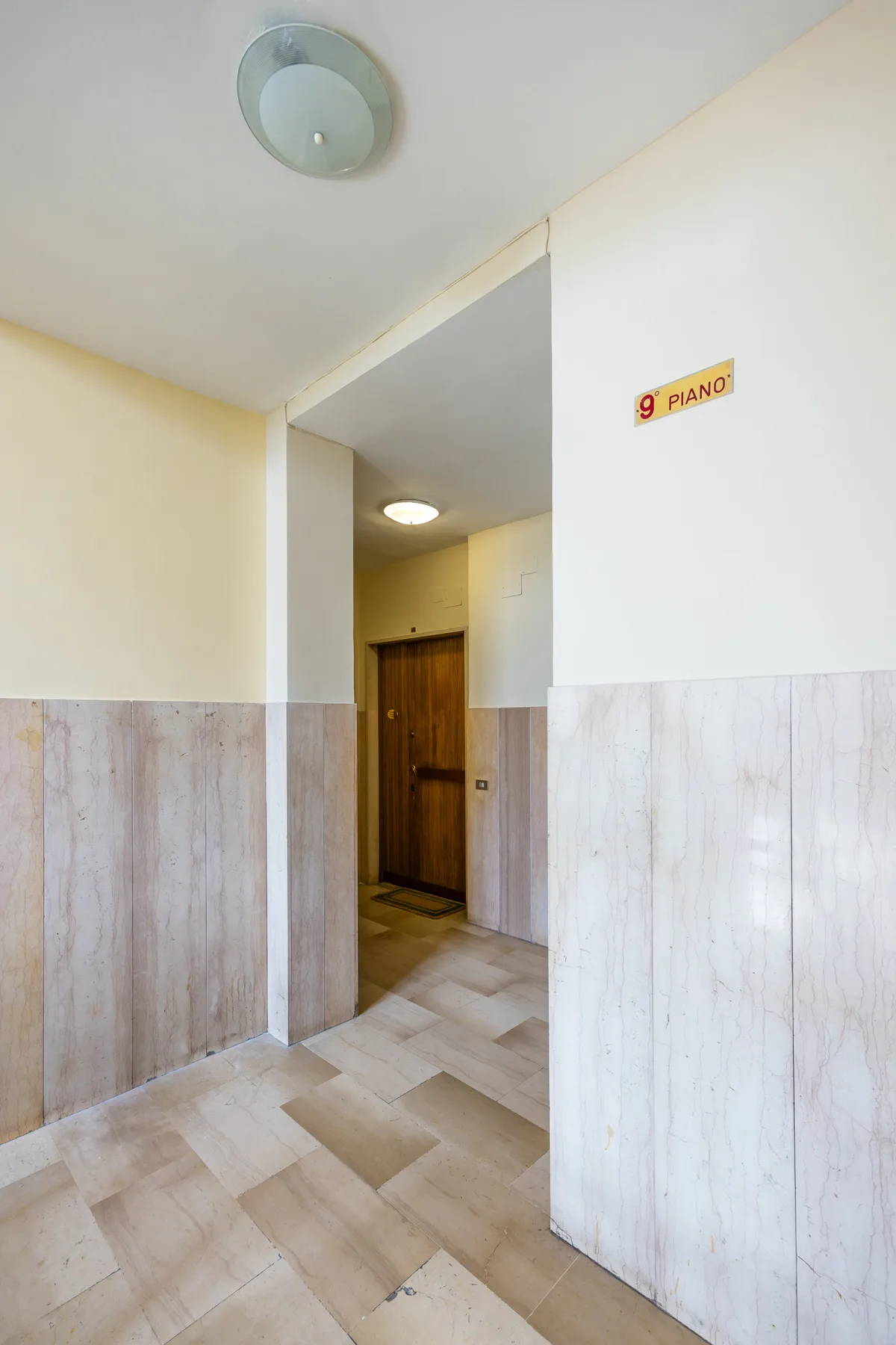 A building hallway with a wooden door and light-colored tiled walls.
