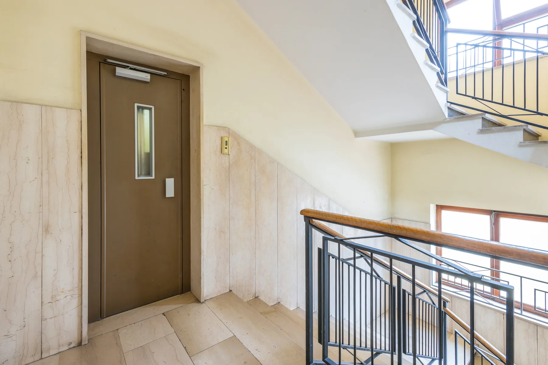 An indoor stairwell landing with a brown door and metal railings.