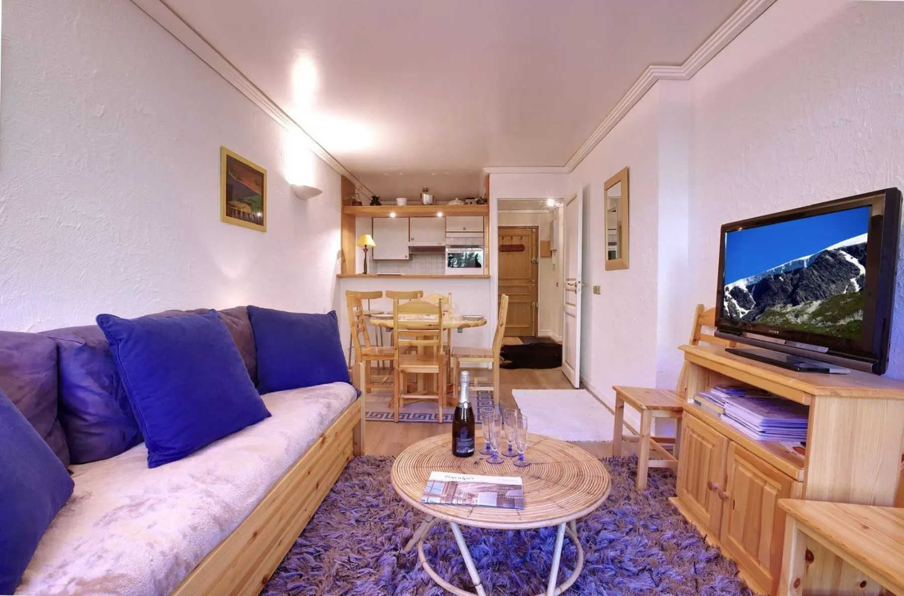 A living room with seating, a television, and a dining table in the background.