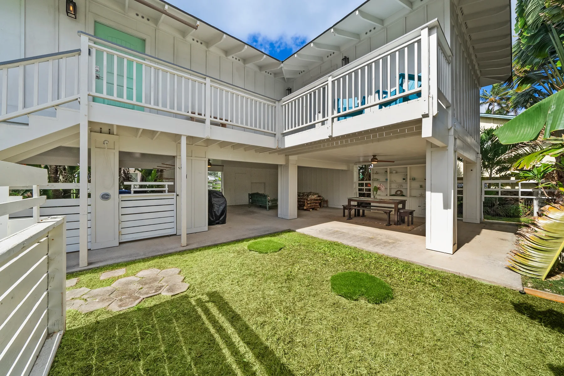 Una casa blanca elevada da a un patio con césped y una zona cubierta bajo la terraza.