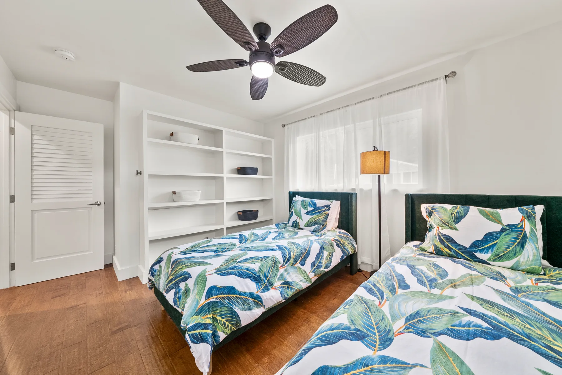 Un dormitorio luminoso con dos camas vestidas con ropa de cama estampada con hojas azules y verdes.
