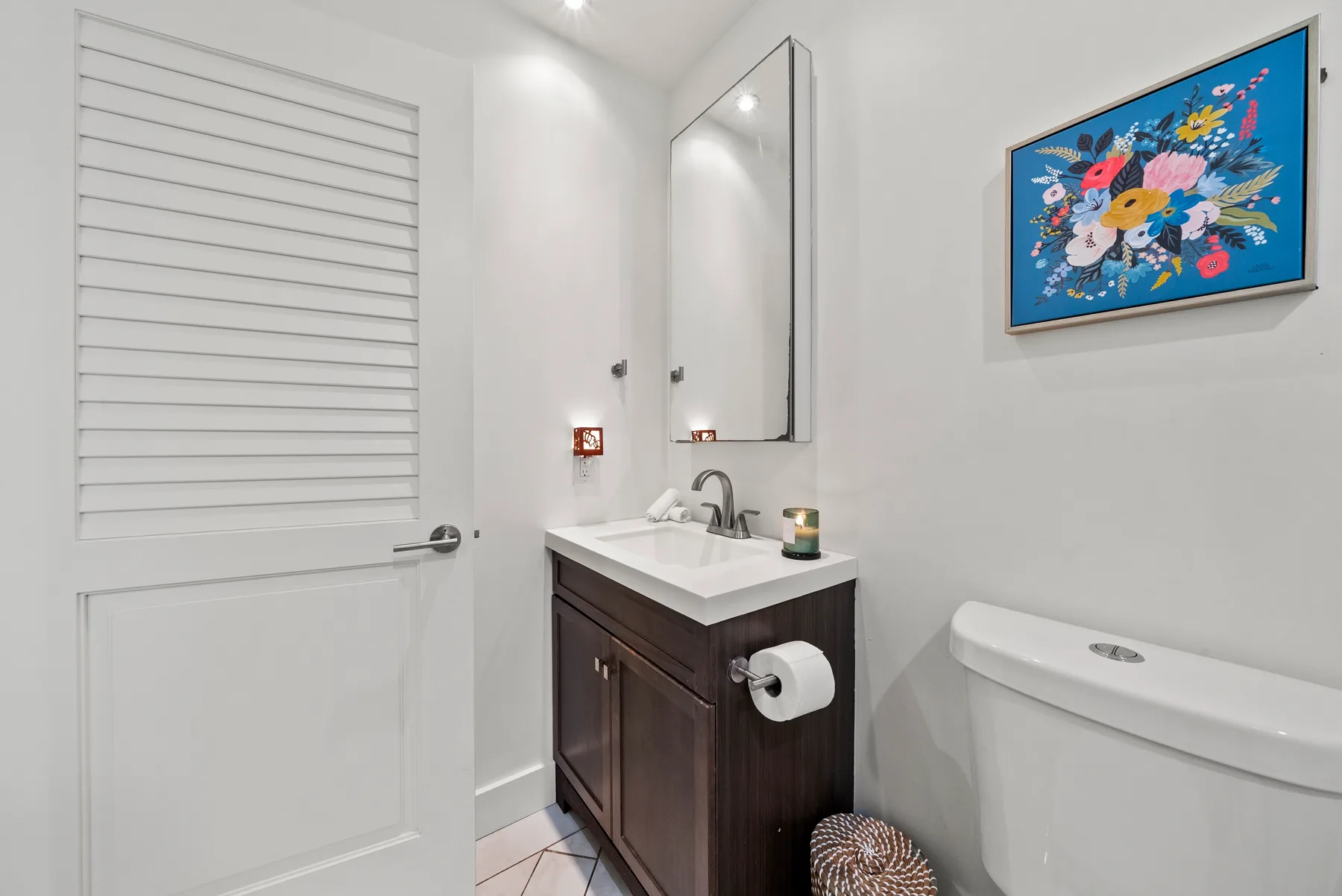 Un baño con lavabo y mueble, inodoro y una lámina floral enmarcada.