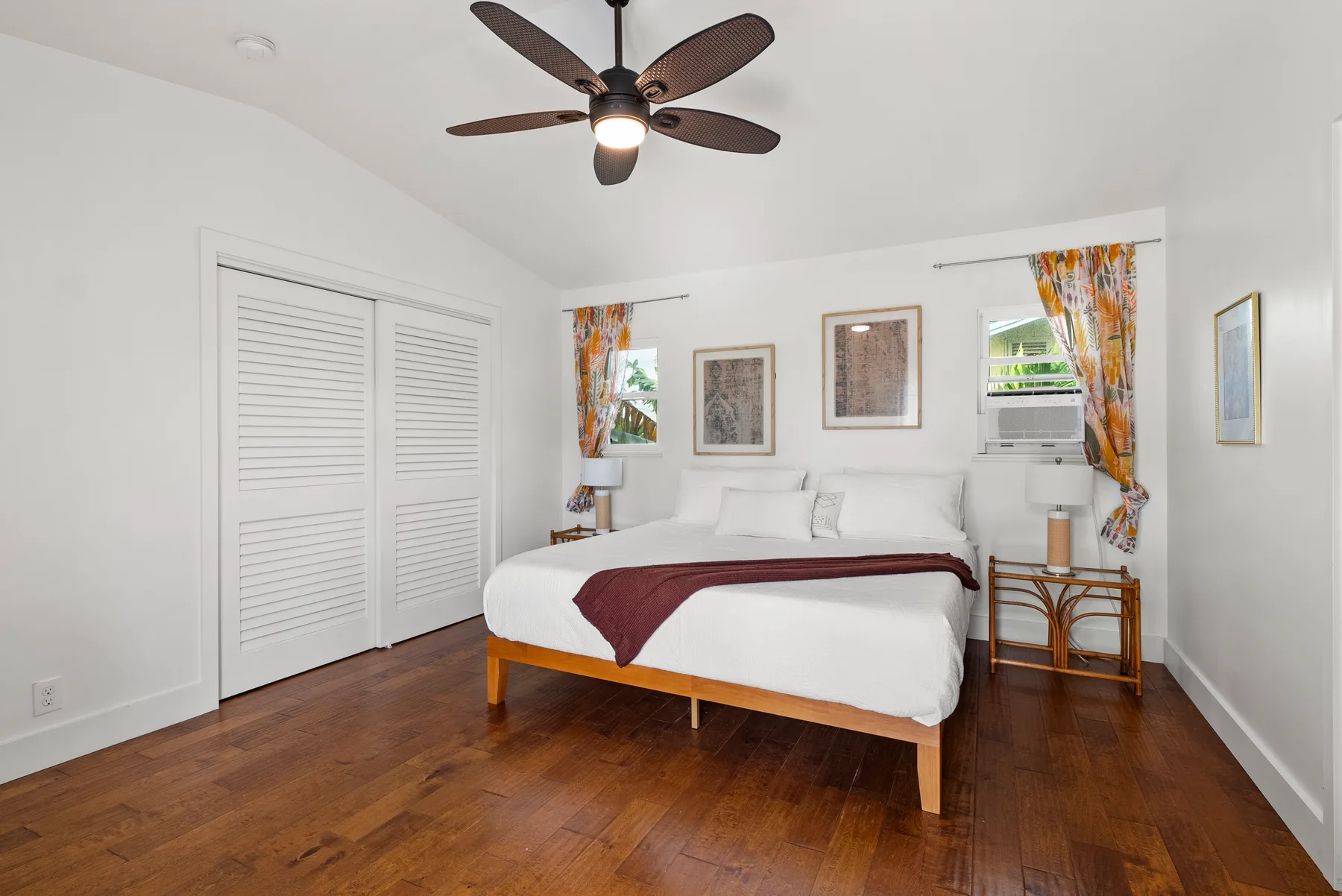 Un dormitorio luminoso con una cama bien hecha, cortinas coloridas y suelo de madera.