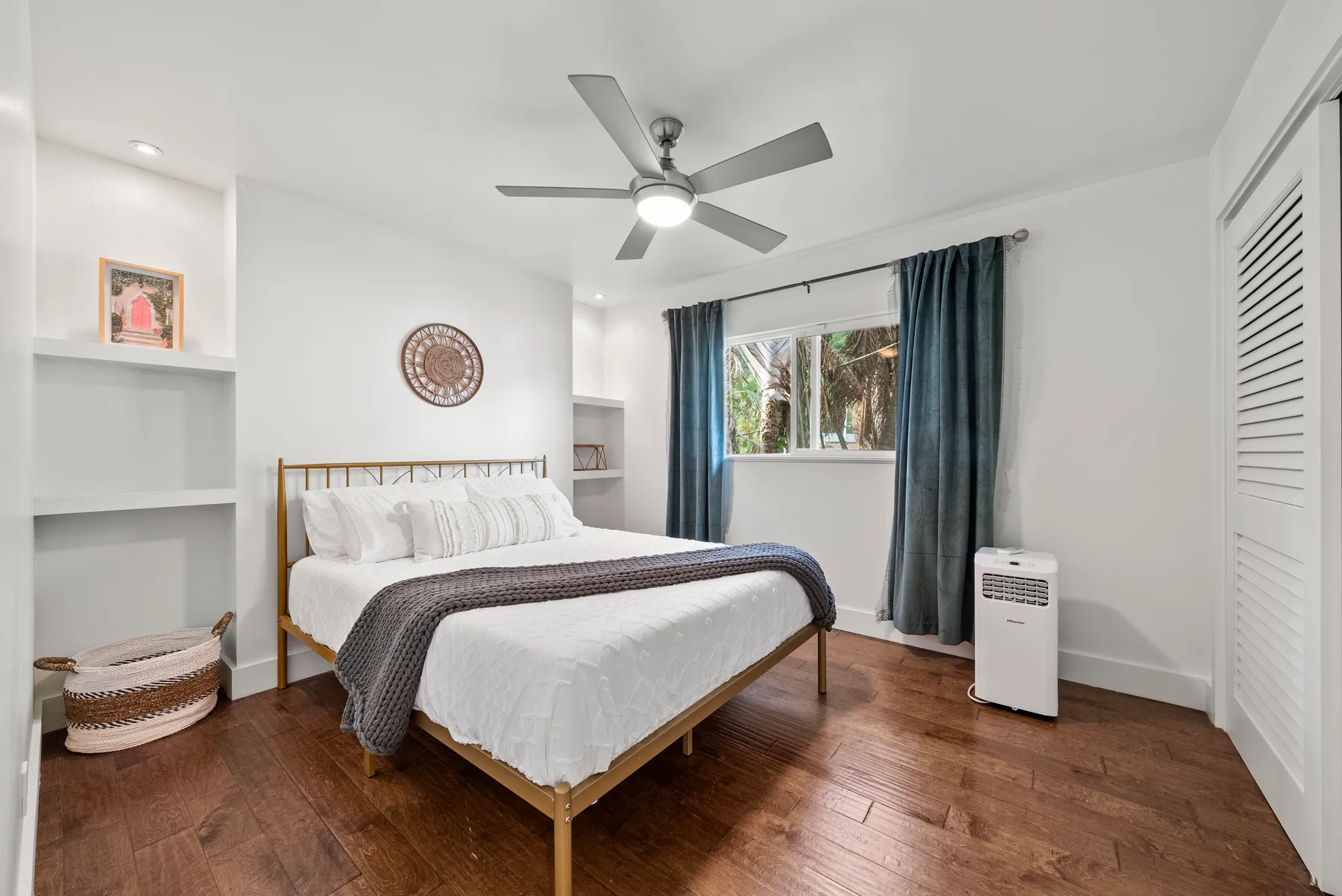 Un dormitorio luminoso con una cama, estantes empotrados y una ventana con cortinas.
